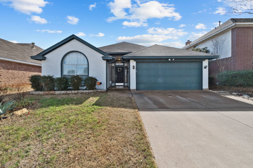 Exterior of home is white with navy accents and garage door. One story home with large front window.